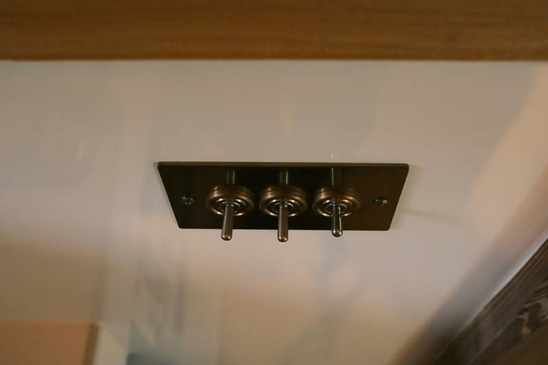 Close-up of four popular smart switches (Lutron Caseta, TP-Link Kasa, Leviton Decora, and Eve Light Switch) arranged neatly on a well-lit wood workbench beside wire strippers and a voltage tester